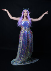 Sticker - Full length portrait of beautiful female model with long purple hair wearing elf ears, a fantasy fairy crown and  rainbow glitter sequin ball gown. graceful standing pose,  isolated in dark studio bac