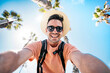 © Davide Angelini - Happy tourist taking self portrait outside with cellphone on summer vacation - Handsome young man laughing at camera enjoying summertime day out - Tourism, traveler life style and technology concept