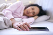 © peopleimages.com - Sleep, woman and bedroom with hand on phone to snooze alarm, alert and notification for tired, relax and dream. Fatigue, young female and exhausted from insomnia with mobile for time in morning