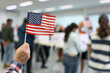 close-up of the moment of patriotism as a person holds an American flag while standing in line at the ballot box. With fellow voters in the background casting their votes, the imag