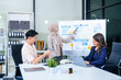 © Phushutter - A multicultural team of professionals, including male and female businesspersons, convenes around a desk with tablets, discussing strategies illustrated on a whiteboard during a dynamic presentation.