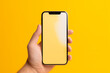 © Canary - hand holding smartphone in an isolated yellow background. Empty screen smartphone for a mockup. AI generated