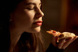 A beautiful girl with her eyes closed enjoys eating pizza. Lips are painted with red lipstick.