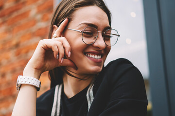 Wall Mural - Cheerful female journalist laughing and feeling excited after well done interview sitting with textbook outdoors, happy smiling hipster girl in eyeglasses for vision correction enjoying life