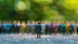 © Bnz - Single male figurine standing before blurred crowd, concept of leadership and individuality in society.