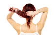 Rear of a young woman tying her long red wavy hair on a white background