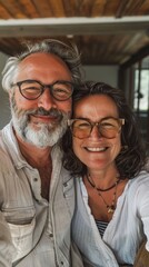 A joyful couple with glasses smiling for the camera in a rustic setting.