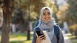 © The Little Hut - Cheerful Arab Female Student With Smartphone And Workbooks Standing Outdoors Happy Young Middle Eastern Woman Walking In City After College Classes Looking Away And Smiling Copy Space : Generative AI