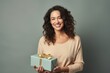 © Markus Schröder - Portrait of a smiling woman in her 30s holding a gift in front of pastel gray background