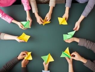 Group of hands folding yellow and green paper boats on a table. Simple, creative, and colorful activity. Focus on hands and origami process, representing teamwork and fun.