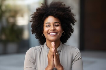 Wall Mural - Portrait of a jovial afro-american woman in her 40s joining palms in a gesture of gratitude while standing against pastel gray background