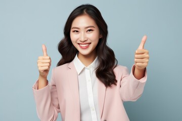 Wall Mural - Portrait of a glad asian woman in her 20s showing a thumb up over pastel gray background