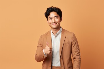 Canvas Print - Portrait of a content asian man in his 30s showing a thumb up isolated in pastel brown background