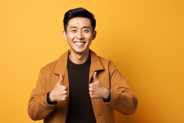 Wall Mural - Portrait of a content asian man in his 30s showing a thumb up in front of pastel brown background