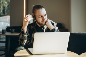 A man with a cup of coffee sits in front of a laptop in a cafe in the morning.