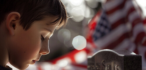 Wall Mural - Boy's face focused in prayer at a tombstone with an unfocused US flag draped behind.