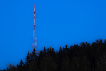 A tall communication tower painted red and white stands against a clear blue sky, emphasizing its towering presence.