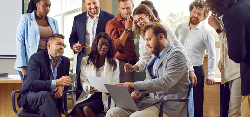 Wall Mural - Team of diverse business people meeting in office, working on project and using laptop. Group of young and mature mixed race male and female employees looking at notebook computer all together