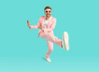 Full body portrait of a happy cool casual young funny man with unshaven beard wearing bright pink suit and modern sunglasses having fun isolated on a blue turquoise studio background.