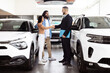 © Prostock-studio - A professional car salesman, dressed in a suit, is shaking hands with a happy Indian couple customers inside a car dealership showroom