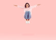 Happy young woman with outstretched arms jumping on trampoline. Overjoyed excited girl jumping up, spreading hands, smiling and flying high in air. Full body length, plain light pink color background
