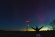 A happy girl watches the northern lights in nature near a wind generator, night photo, rear view.