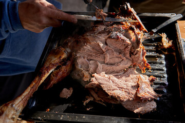 man's hands cutting a leg of lamb with a knife on a grill in Argentina