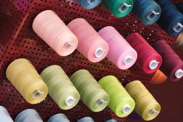 Aufkleber - A rack of colorful spools of thread. The spools are arranged in a row, with some being green, pink, and yellow. The spools are all different sizes and colors, creating a vibrant and lively atmosphere