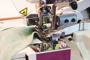 Leinwandbilder - A sewing machine is in use, with a green cloth being sewn. The machine has a yellow warning label on it