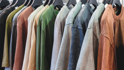 Poster - A row of shirts hanging on a rack, with some being green and others being brown. The shirts are all different colors and styles, and they are all hanging on the same rack
