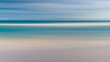 Fototapeta  - A blurry image of a beach with a blue ocean and white sand. The image has a dreamy, ethereal quality to it, as if it were a painting rather than a photograph. The water appears to be calm and still