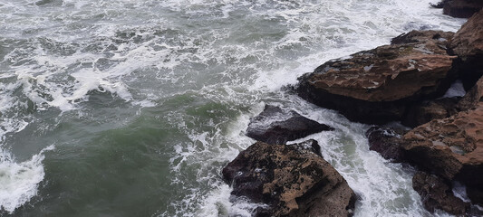 Wall Mural - The waves of the sea are crashing against the rocks on a stormy day, creating a dramatic and powerful scene.