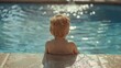 © Emiliia - A young baby is sitting in a pool, looking intently at the clear water in front of them.