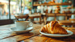 Coffee cup and croissant on wooden table in coffee shop