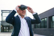 © Koldo_Studio - A corporate leader in a suit using virtual reality glasses outside a modern urban office building.