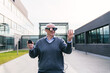 © Koldo_Studio - A senior executive wearing a sweater engages with virtual reality glasses, interacting with virtual elements outside a modern office building
