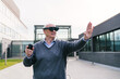 © Koldo_Studio - Senior executive using virtual reality glasses and a controller, interacting with virtual elements outside a modern office building.