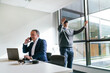 © Koldo_Studio - A businessman makes a call on his laptop while his colleague interacts with VR technology in a modern office setting