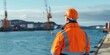 © kiimoshi - worker in orange uniform and safety helmet standing on pier and looking at docked cargo ship