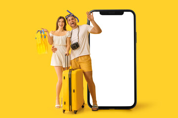 Canvas Print - Beautiful young happy couple of tourists with suitcase, flippers and snorkeling mask on yellow background