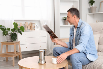 Sticker - Mature man with cup of hot coffee reading magazine on sofa at home