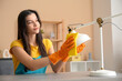 © Pixel-Shot - Young woman cleaning lamp with rag in living room