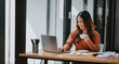 © Satori Studio - A woman is sitting at a desk with a laptop and a cup of coffee. She is smiling and she is enjoying her work