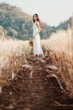 © Satori Studio - A woman is standing in a field with a straw hat on. She is wearing a white dress and is smiling