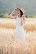 © Satori Studio - A woman is standing in a field of tall golden wheat. She is wearing a white dress and a straw hat. She is smiling and she is enjoying the moment