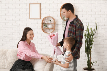 Poster - Father with son greeting his mother with Mothers Day with bouquet of tulips and gift in living room