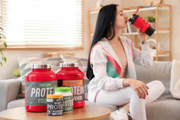 Canvas Print - Jars with protein powder on table of sporty woman drinking shake at home, closeup