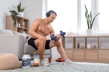 Canvas Print - Young muscular man in headphones with dumbbell and protein powder training at home