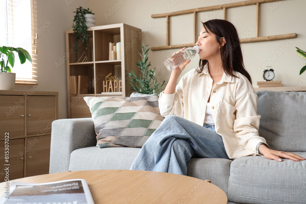 Young Asian woman drinking water on sofa at home