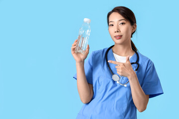 Wall Mural - Female Asian doctor pointing at bottle of water on blue background